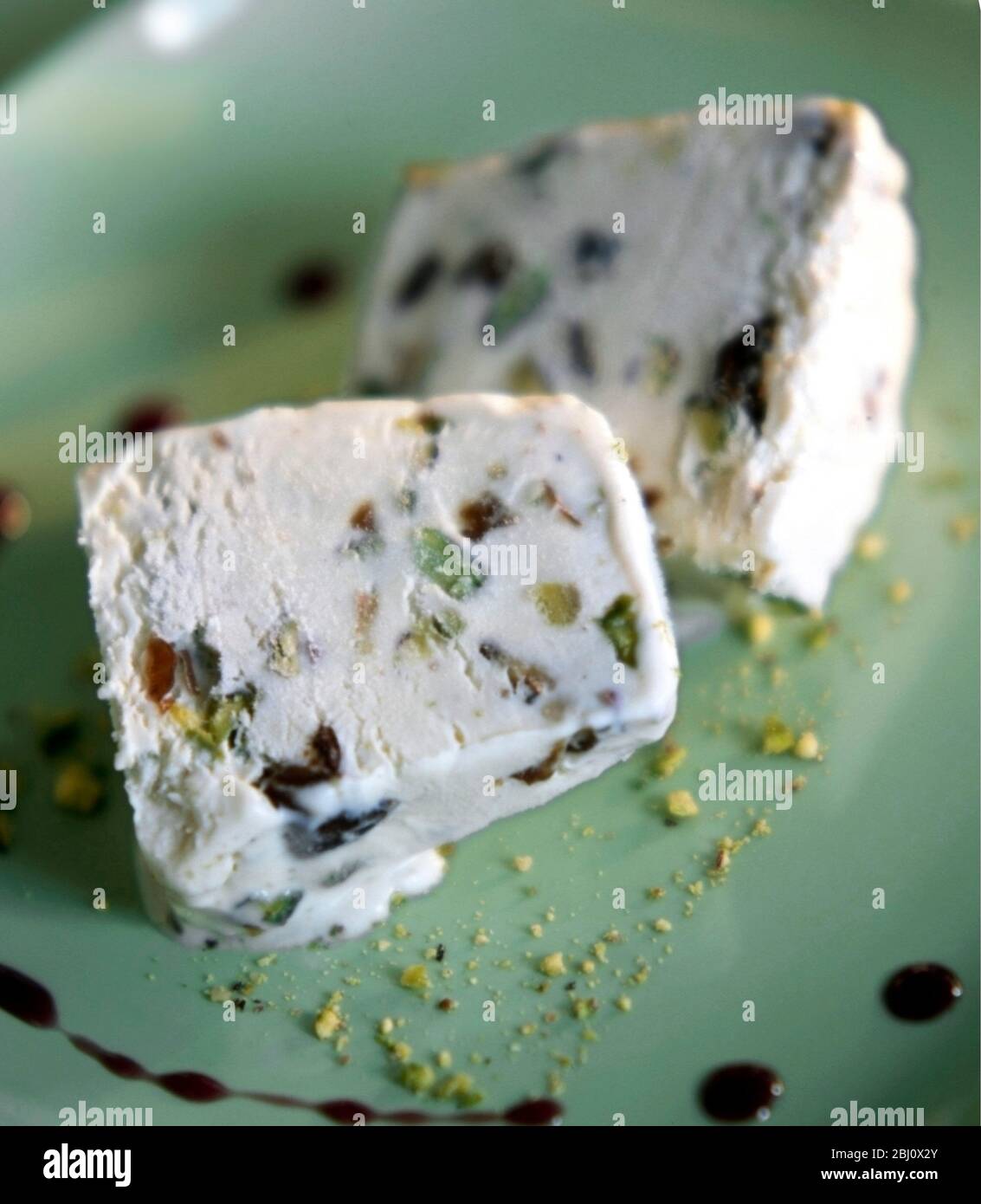 Helado de pistacho casero en plato verde con frutos secos picados y salsa de chocolate con perrera - Foto de stock