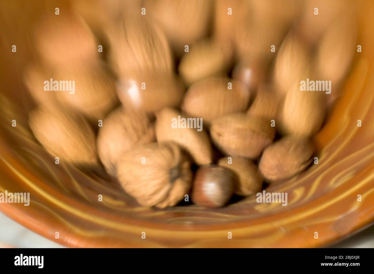 Cuenco cerámico de barro marrón de frutos secos mezclados en sus conchas. Grabado con lente de lensbabies - Foto de stock