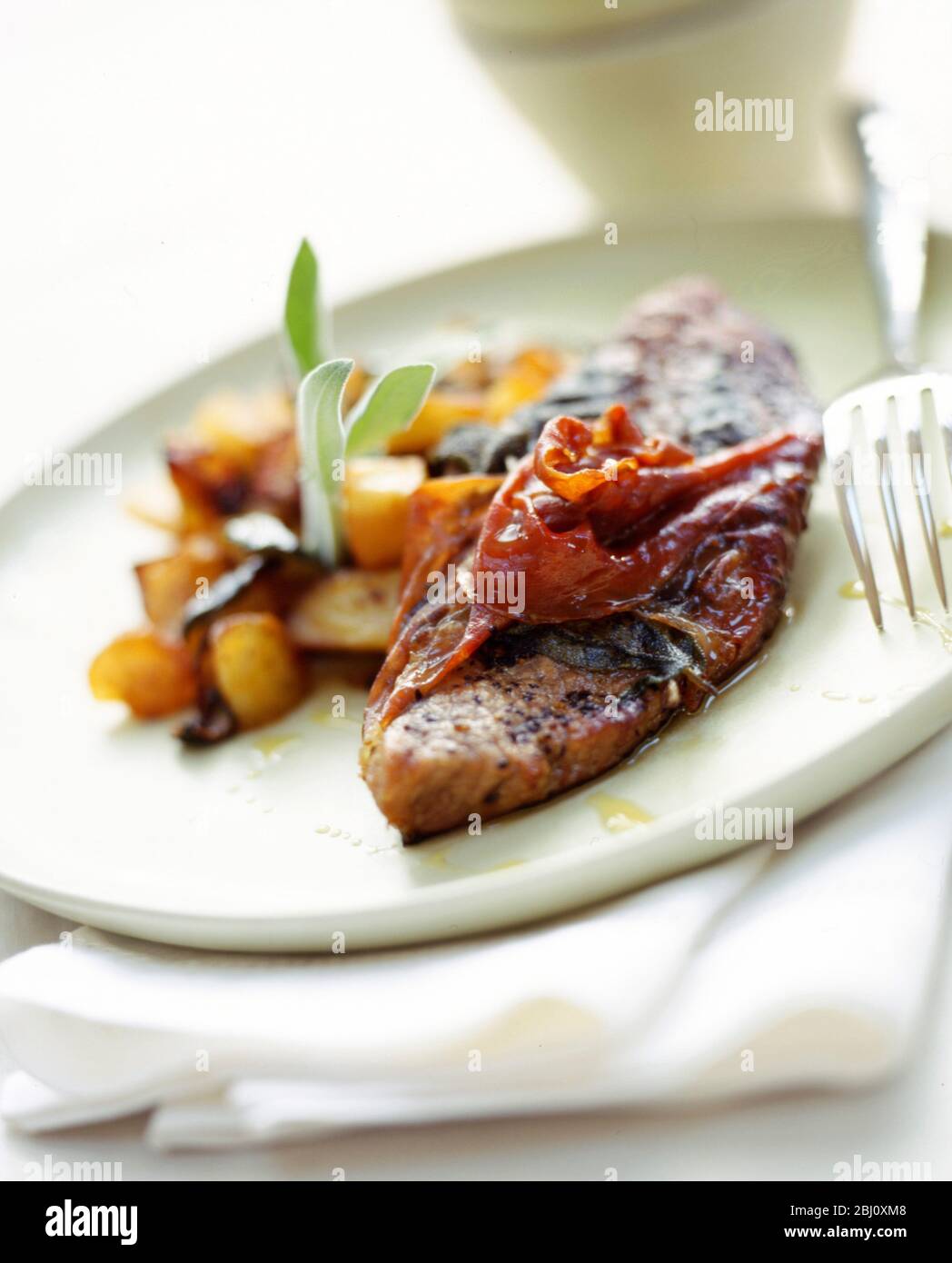 Filetes de cerdo fritos en sartén envueltos en tocino y servidos con patatas salteadas adornadas con salvia en plato verde pálido - Foto de stock