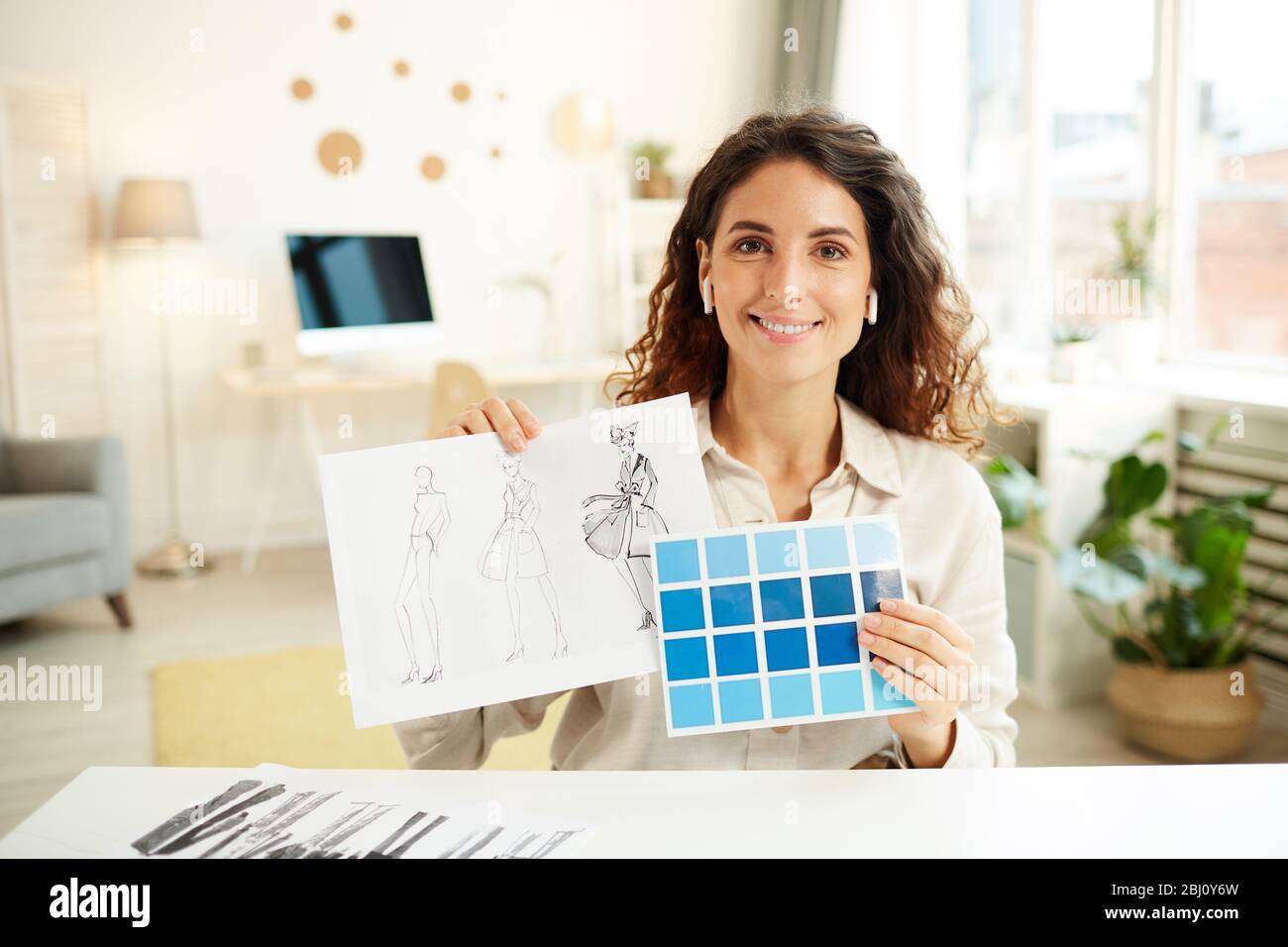 Diseñadora de ropa femenina que muestra bocetos y paleta de colores azules en la cámara, retrato horizontal medio Foto de stock