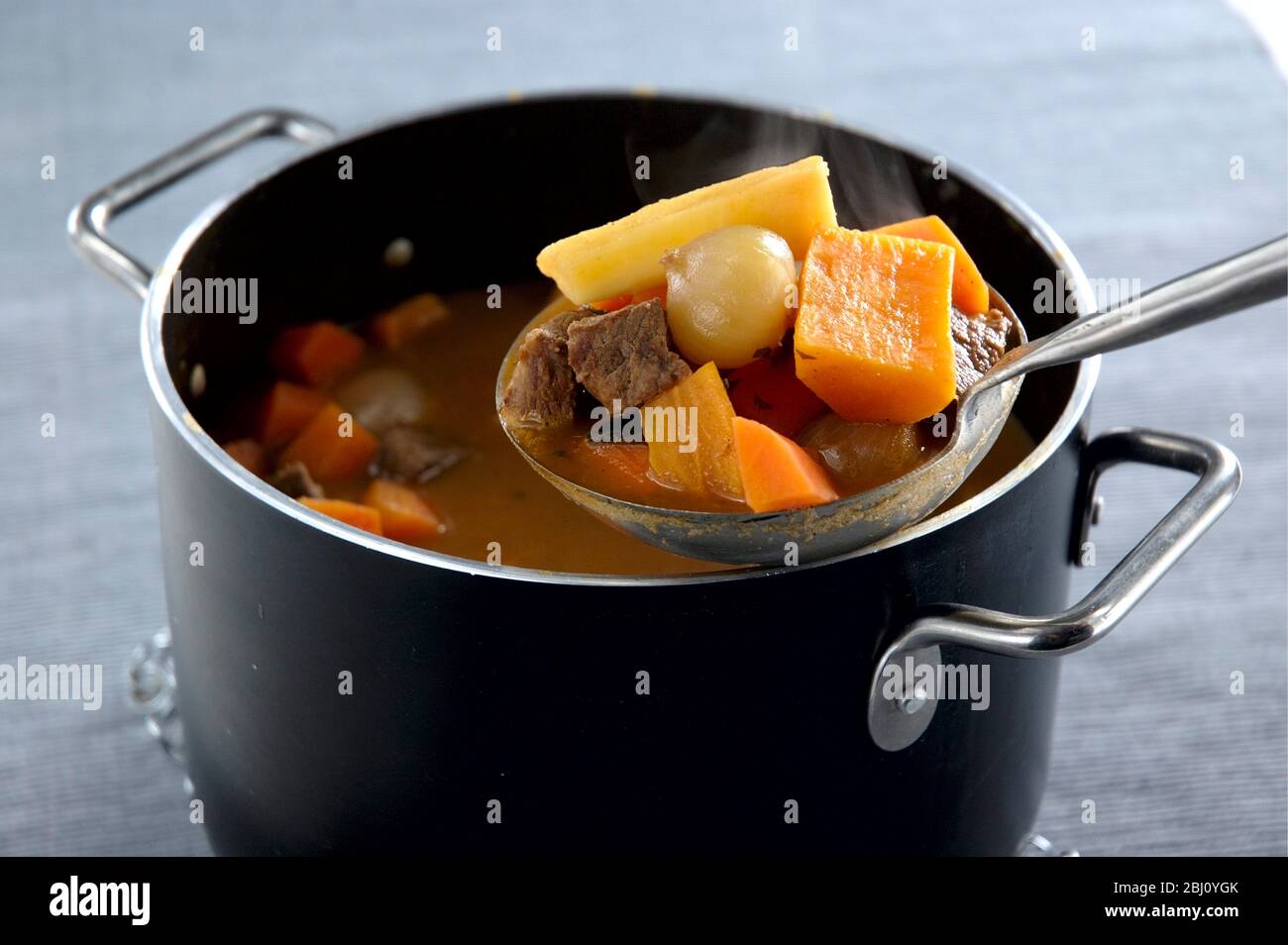 Estofado de ternera con verduras de raíz con una cuchara que se utiliza para servir una porción - Foto de stock
