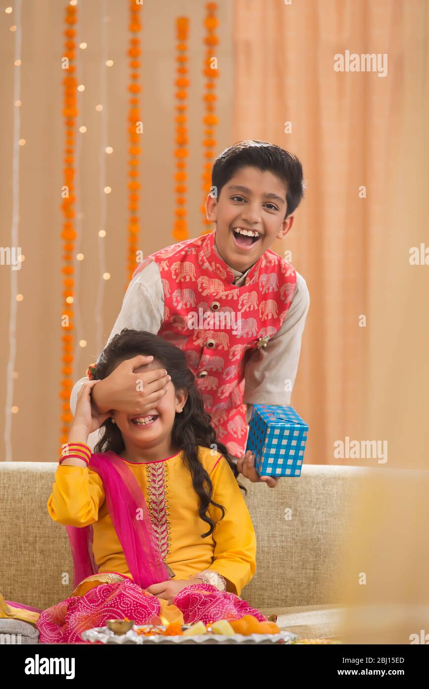 Hermano sorprendiendo a su hermana pequeña y linda con un paquete de regalo en Rakshabandhan Foto de stock