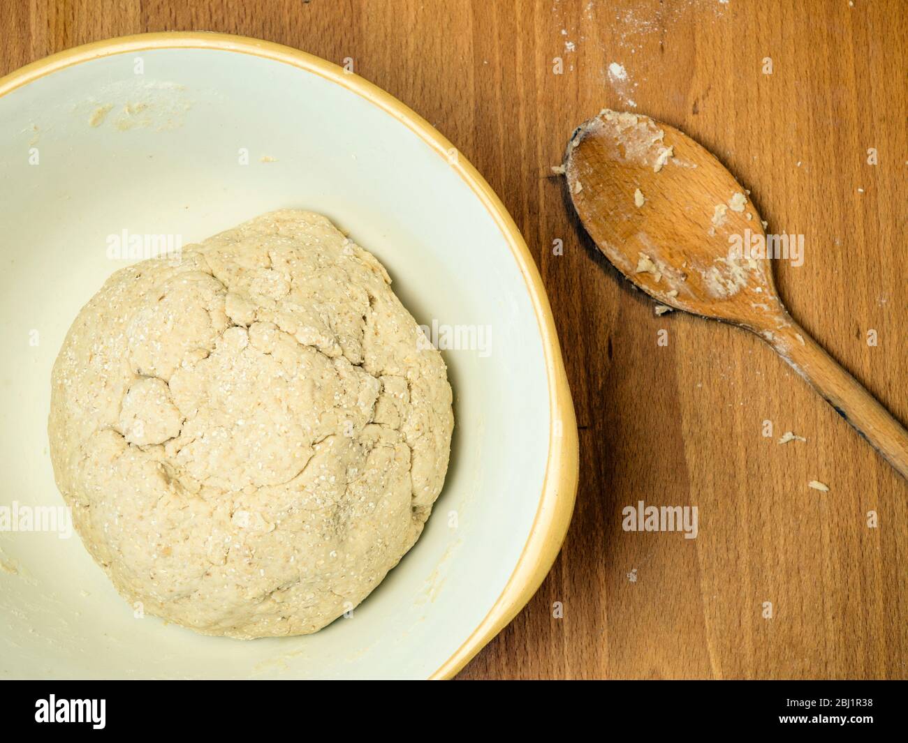 Masa de pan de avena hecha forma de harina de pan blanca fuerte con espuma de avena y avena enrollada en un cuenco para mezclar con una cuchara de madera Foto de stock