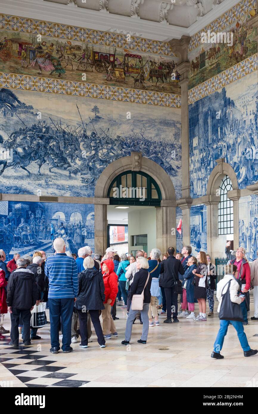 Los turistas admirando los famosos azulejos tradicionales portugueses azulejos azules y blancos de la pared estación de tren Sao Bento en Oporto, Portugal Foto de stock