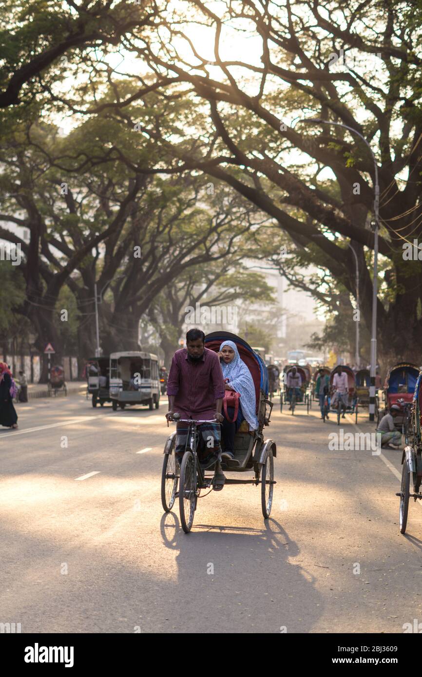 Dhaka / Bangladesh - 14 de enero de 2019: Rickshaw transportando pasajeros en una hermosa calle rodeada de árboles verdes Foto de stock