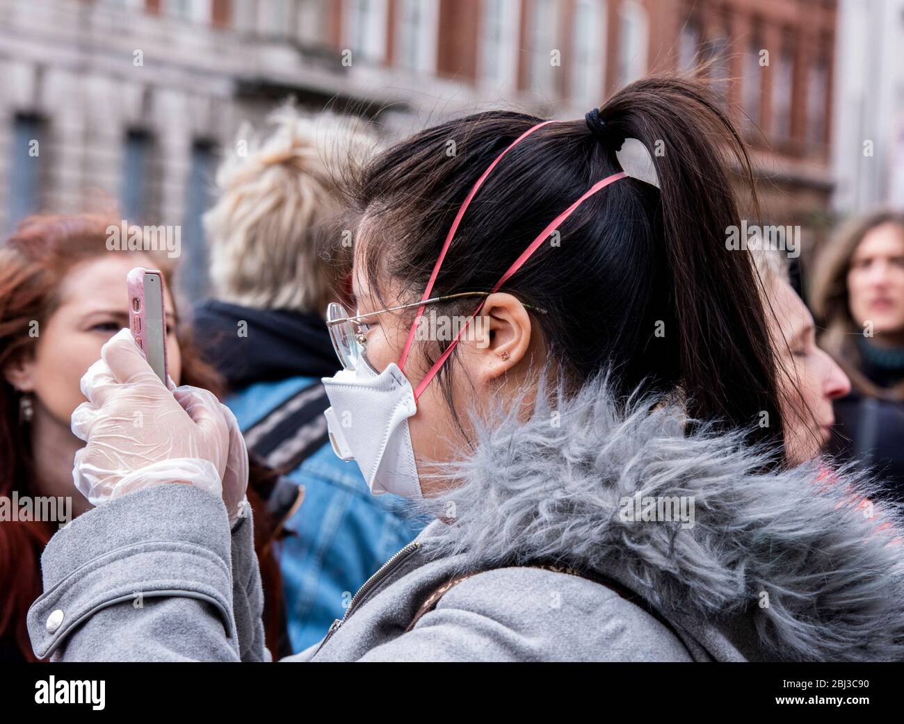 Una joven que lleva una máscara protectora y guantes de plástico se une a la multitud para marcharse hacia la Plaza del Parlamento para celebrar el día Internacional de la Mujer. Foto de stock
