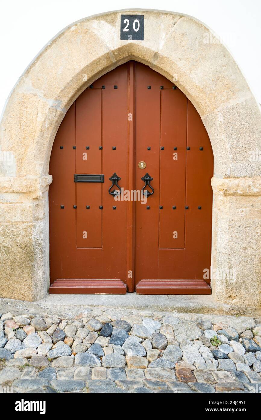 Típica puerta de frente marrón arqueado con postes de hierro forjado y puerta de una casa en una calle de piedra de guijarros en Évora, Portugal Foto de stock