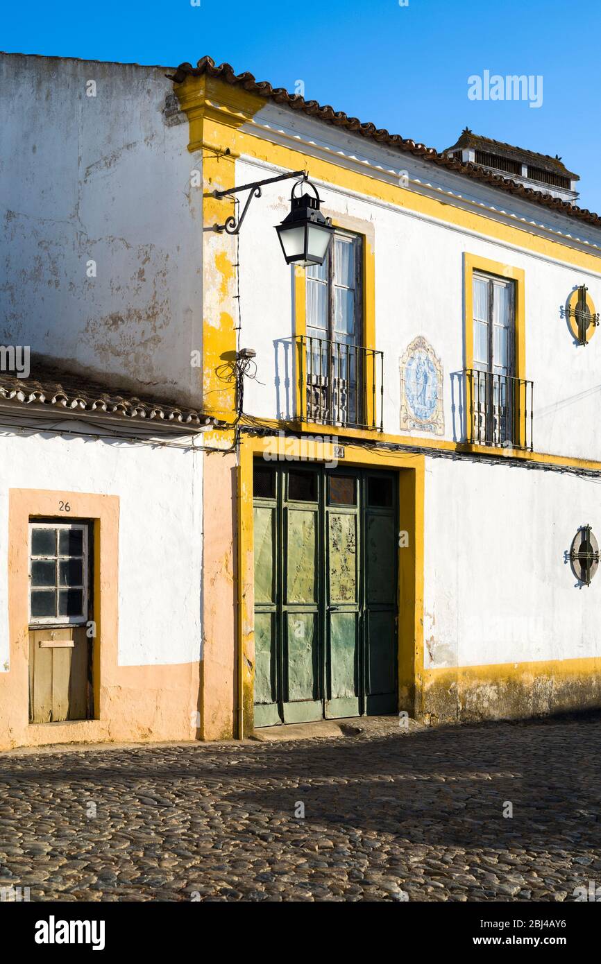 Casa típica blanca y amarilla con balcón, farol, puerta antigua y azulejos azules azulejo de arte religioso en Évora, Portugal Foto de stock