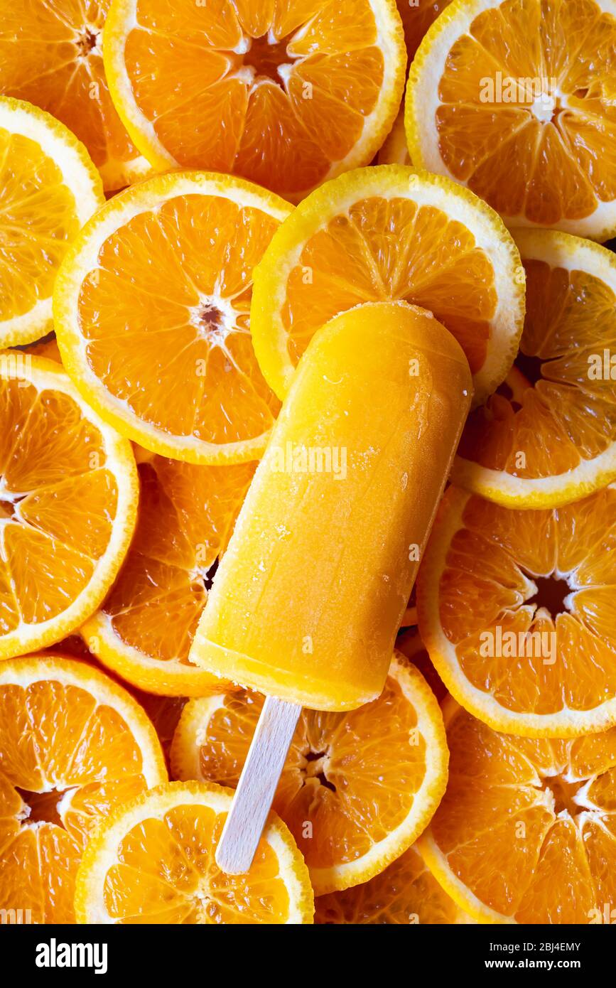 Helado de naranja en un palo. Paletas sencillas sobre un fondo de naranjas cortadas. Sorbete de naranjas en un palo, postre de verano Fotografía de stock Alamy