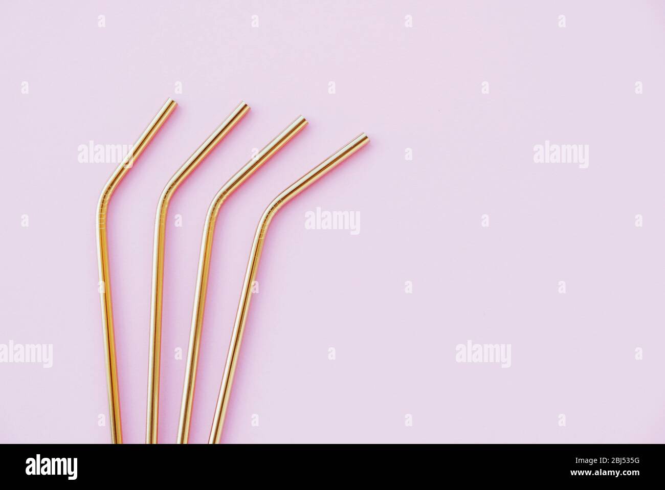 Pajitas de metal doradas reutilizables respetuosas con el medio ambiente sobre fondo rosa pastel. Foto de stock