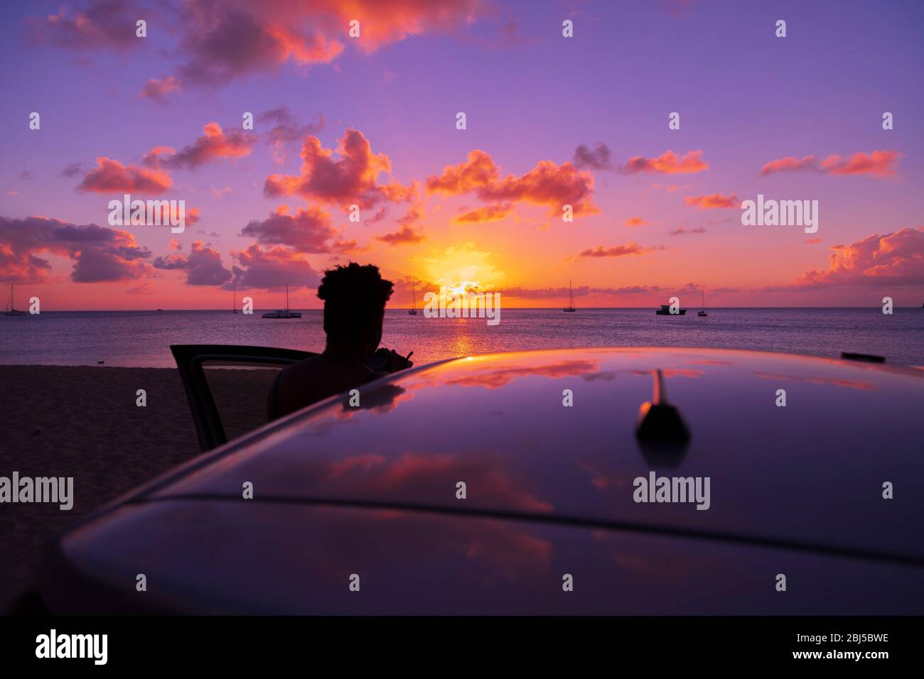 Silueta de una mujer de pie para ver una puesta de sol tropical con la puerta del coche abierta Foto de stock