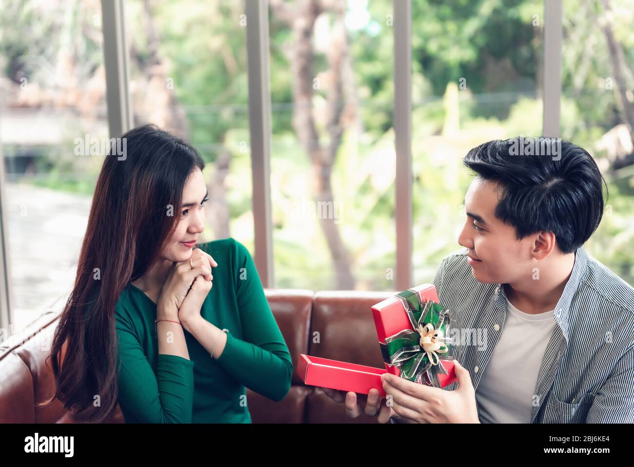 Sorpresa romántica y pareja Amor concepto de San Valentín, joven hombre está presentando sorprendido a su novia en casa. Mujer hermosa que tiene felicidad y. Foto de stock