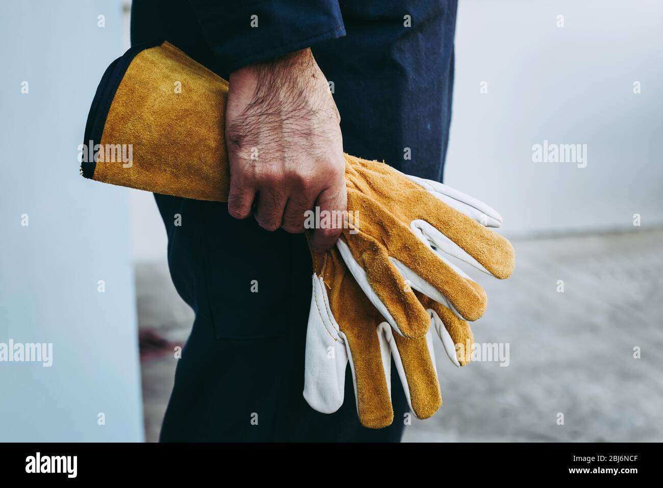 Primer plano de la mano del mecánico técnico sostiene guantes de cuero  mientras está de pie delante del taller de mantenimiento, preparación del  trabajador de servicio técnico f Fotografía de stock 
