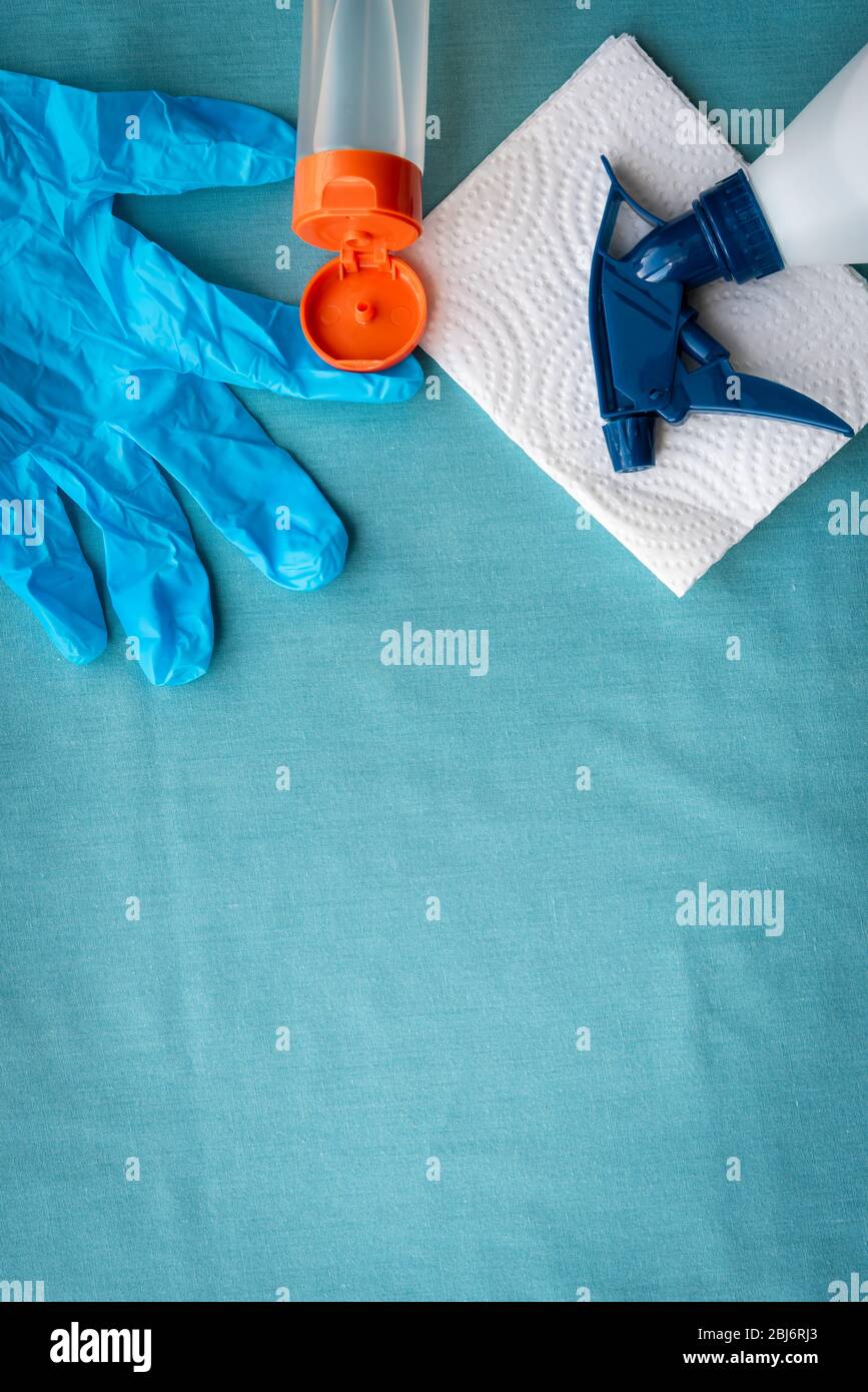 Arreglo plano de guante quirúrgico, botella de desinfectante de manos y spray limpiador sobre fondo azul Foto de stock