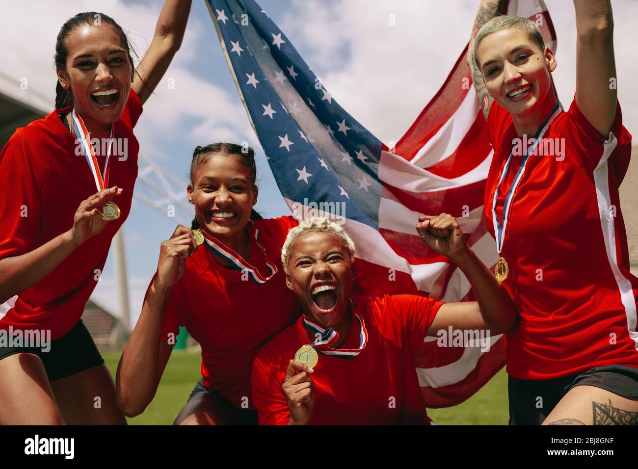 Grupo de equipo femenino de fútbol con medallas que poseen bandera nacional de Estados Unidos en el campo. Equipo de fútbol femenino celebrando la victoria del campeonato. Foto de stock