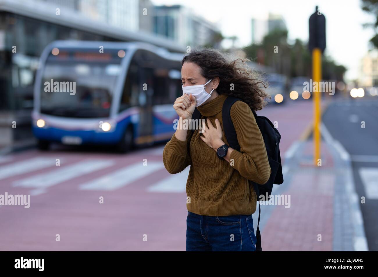 Mujer caucásica con máscara protectora y tosiendo en las calles Foto de stock