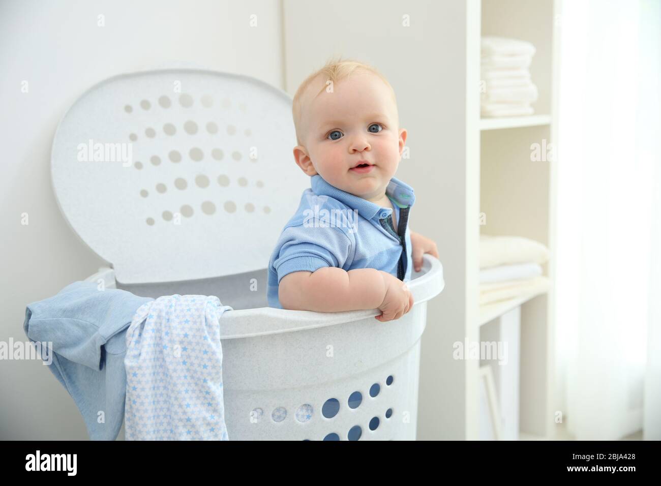 Bastante rubia bebé sentado en un cesto de ropa sucia