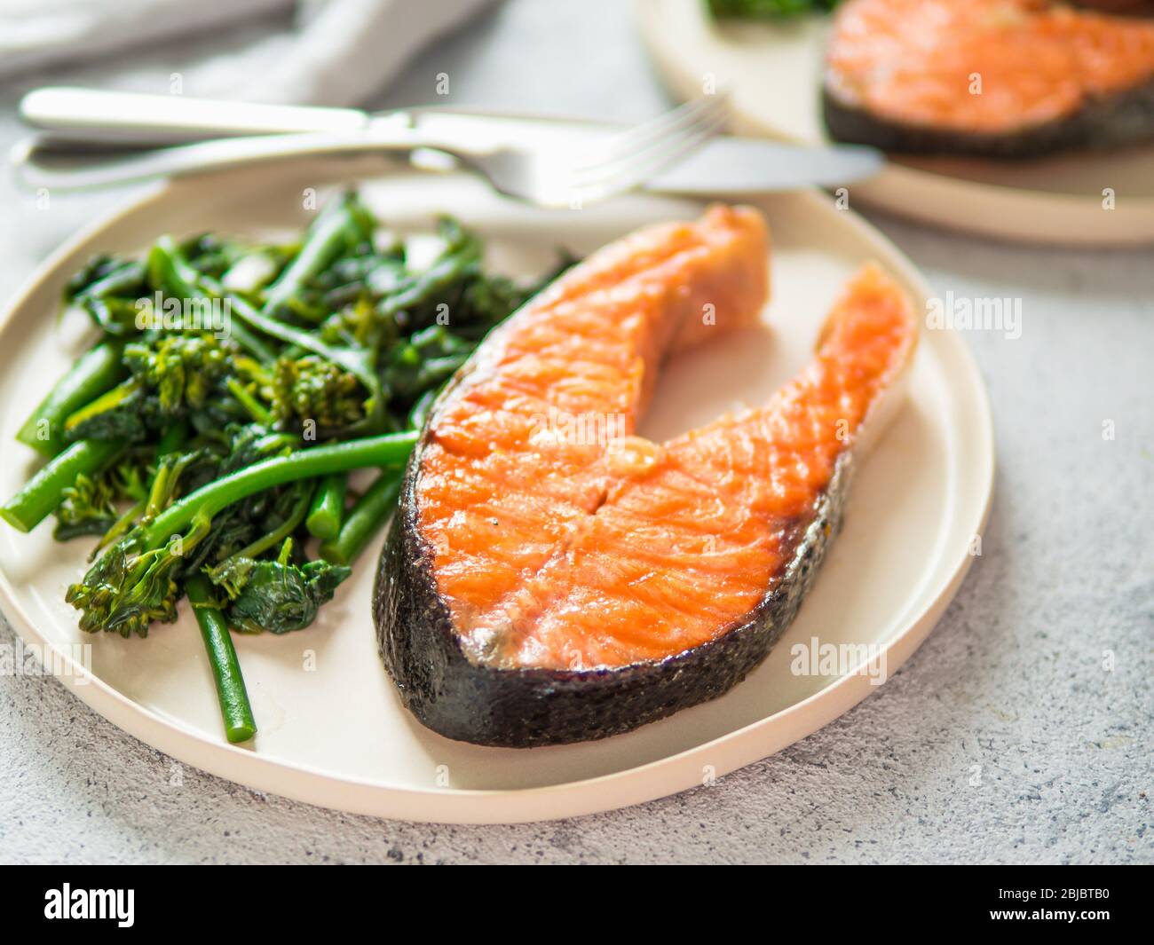 Listo para comer filete de salmón a la parrilla y verdes - baby brócoli o espinacas y broccolini en embarcaciones rústicas placa sobre fondo gris. Dieta ceto plato. Foto de stock