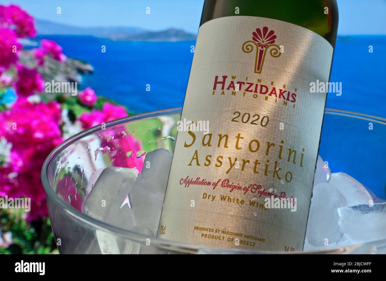 VINO GRIEGO AL AIRE LIBRE Cerrar vista en Hatzidakis Santorini etiqueta de  vino 2020 iluminado por el sol en botella en frío con buganvillas y el mar  de Agean en el fondo