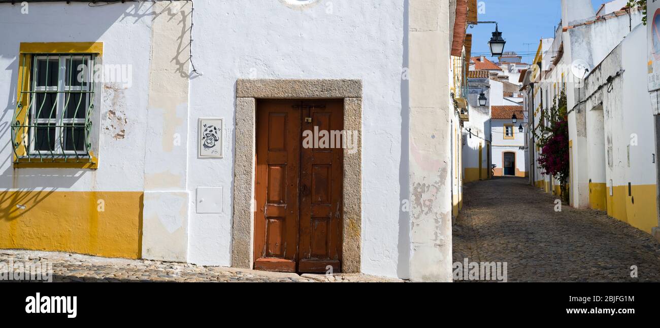 Escena típica de las casas blancas y amarillas, faroles y calle de cobble estrecha en Évora, Portugal Foto de stock