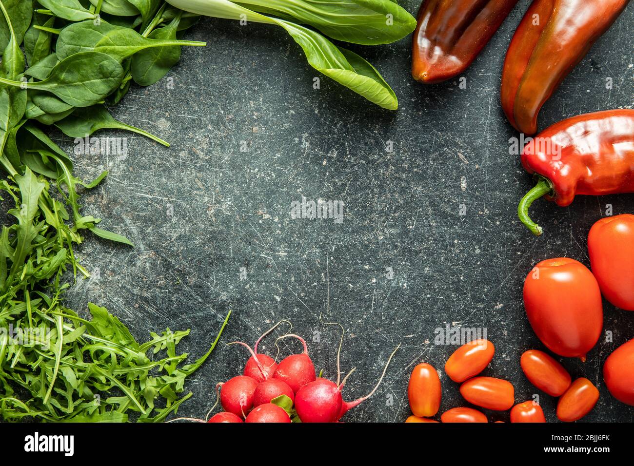 Diferentes verduras. Arúgula, rábanos, espinacas, pimientos rojos, tomates y pak choi en la mesa de la cocina. Vista superior. Foto de stock