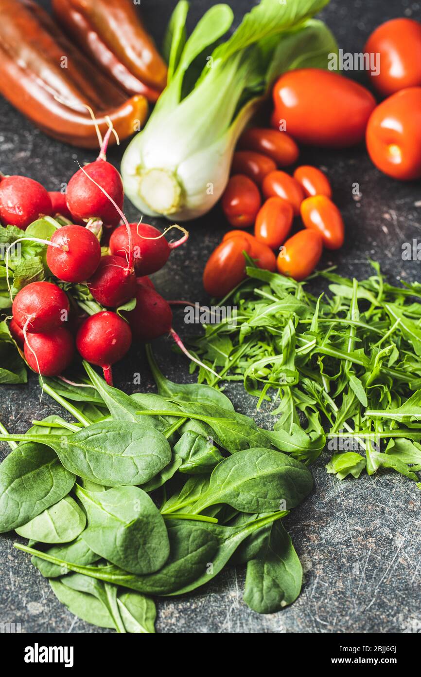 Diferentes verduras. Arúgula, rábanos, espinacas, pimientos rojos, tomates y pak choi en la mesa de la cocina. Foto de stock