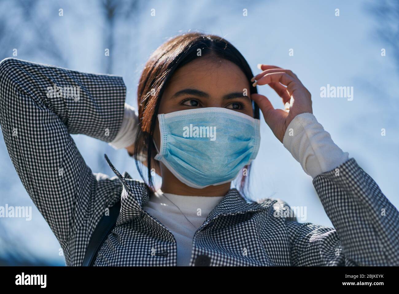 Chica poniendo una máscara protectora para evitar el contagio mientras camina por la calle. Concepto de coronavirus. Foto de stock