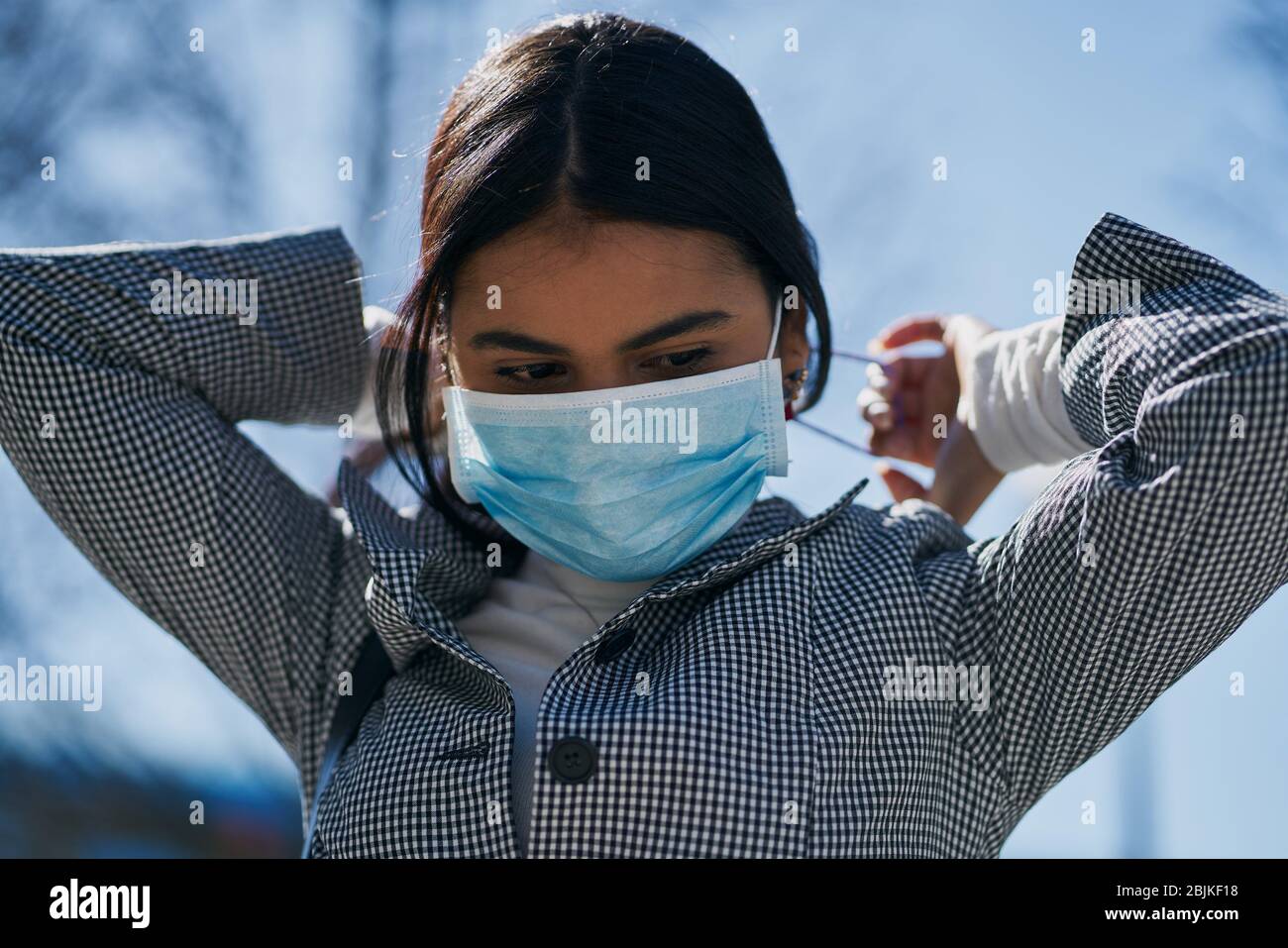 Chica poniendo una máscara protectora para evitar el contagio mientras camina por la calle. Concepto de coronavirus. Foto de stock
