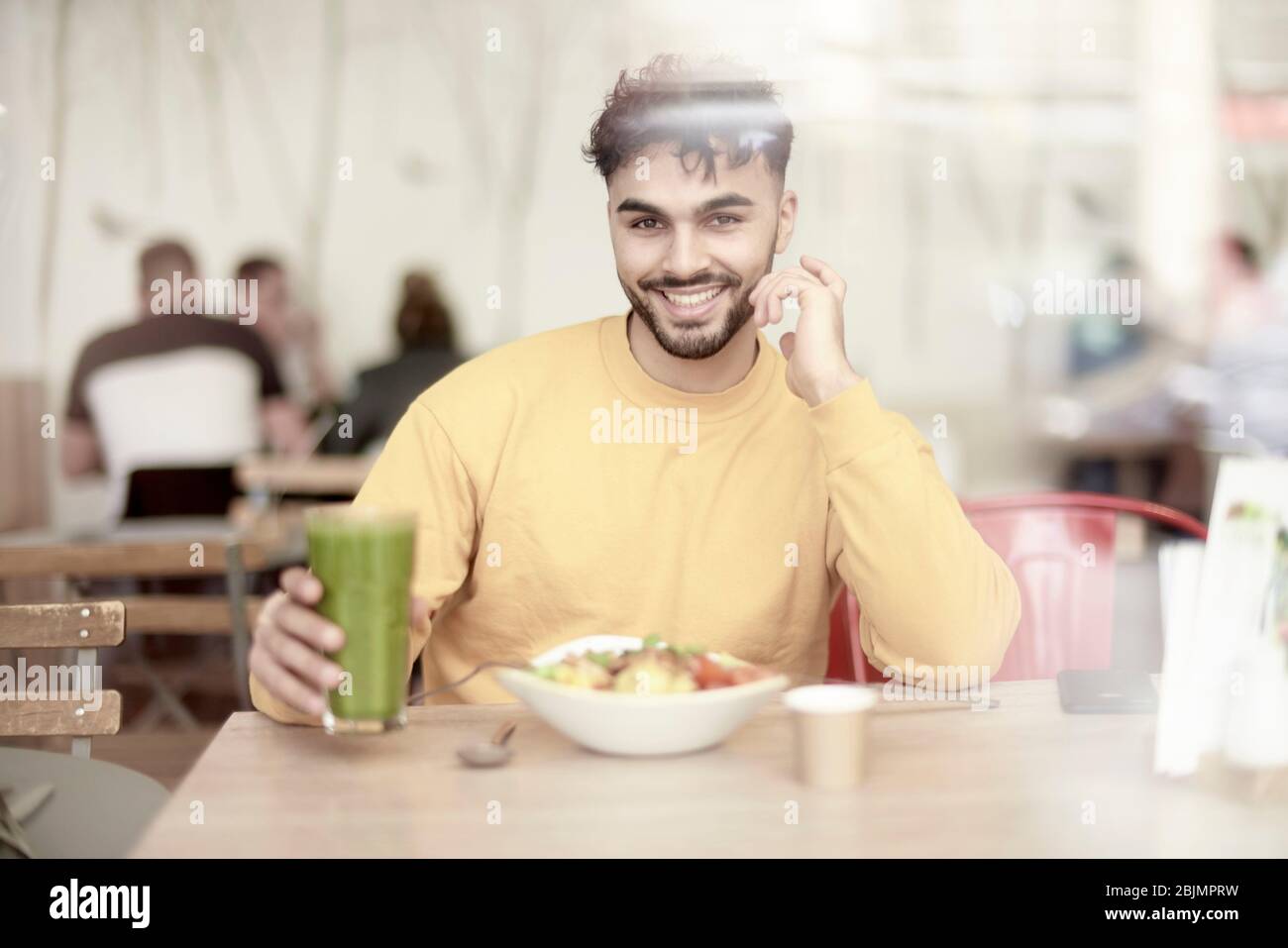 Joven sentado en la mesa del restaurante, comiendo ensalada Foto de stock