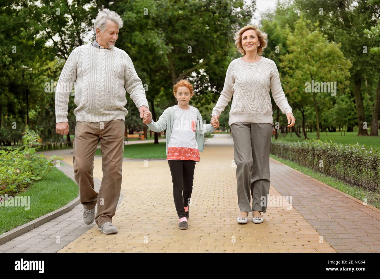 Niña con abuelos caminando en el parque Foto de stock
