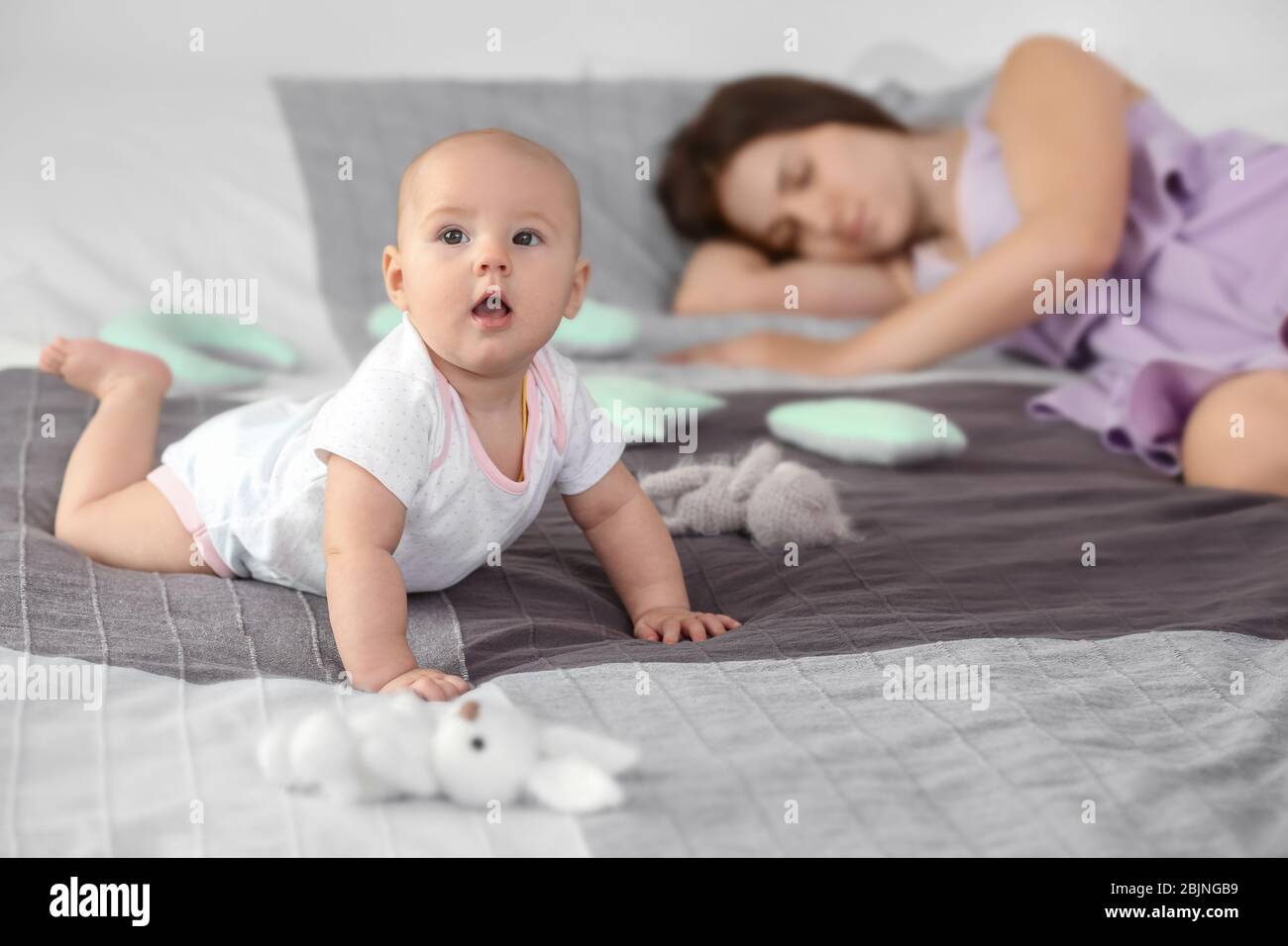 Lindo despertar bebé cerca de la madre dormida en casa Foto de stock