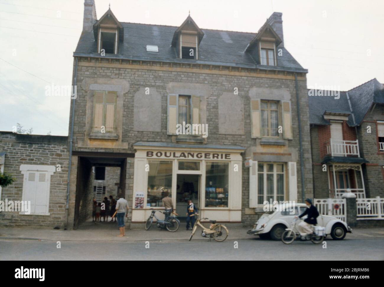 Una mujer en un ciclomotor tradicional pasando por un VW Beetle fuera