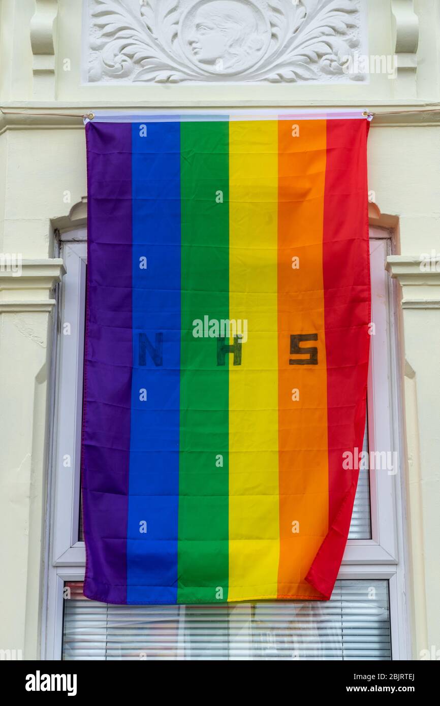 Una bandera arcoiris con la letra NHS en ella volando en la ventana delantera de una casa en apoyo durante Covid-19 Foto de stock
