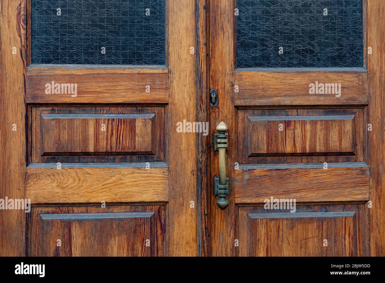 Paneles de doble puerta de madera con ventanas rectangulares y marcos  interiores de vidrio mate. Pomo de puerta retro y abertura de cerradura  antigua en la superficie de madera de la gruñe