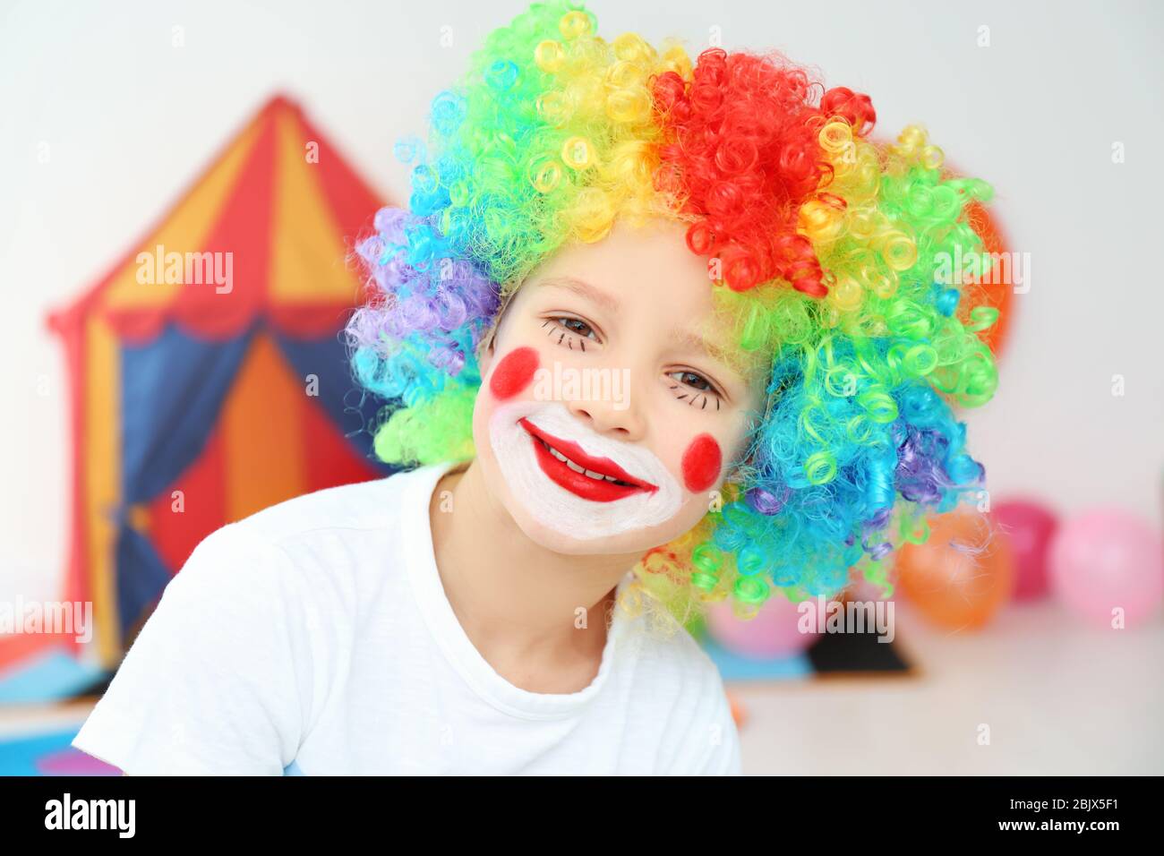 Lindo niño pequeño con maquillaje payaso en la peluca arco iris en el  interior. Abril celebración del día del tonto Fotografía de stock - Alamy