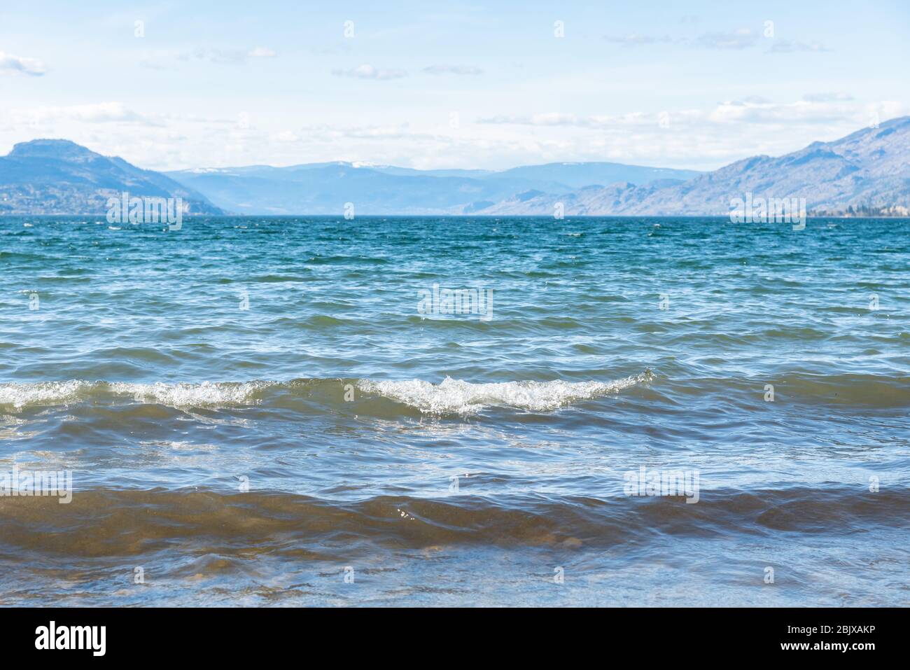 Primer plano de las olas en el lago Okanagan con vistas a las montañas en un día soleado Foto de stock