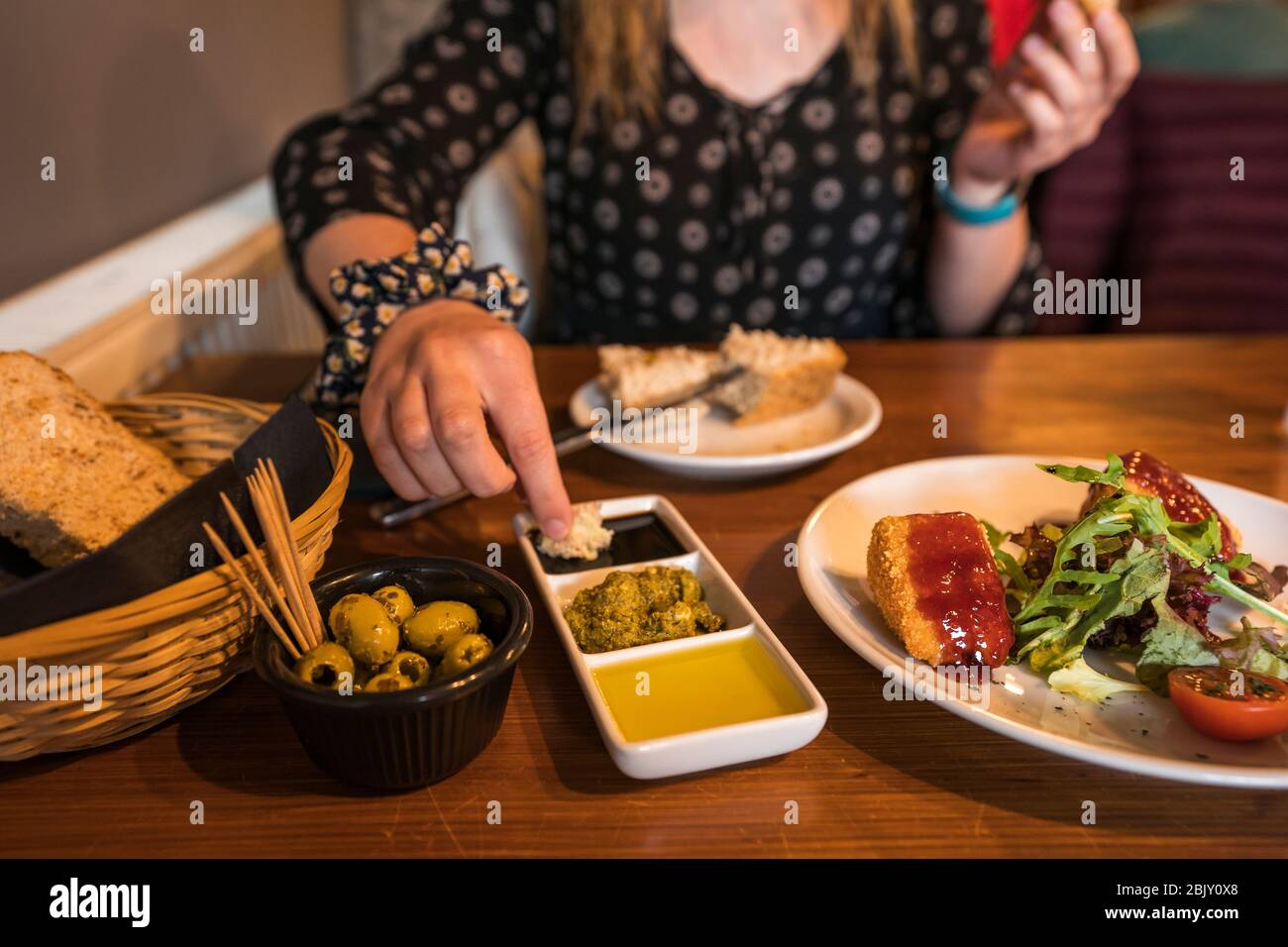 La mujer sumerge el pan en salsa mientras come aperitivos de brie y aceitunas horneadas, vinagre balsámico, aceite de oliva y pesto con pan, Malvinas, Fife, Foto de stock