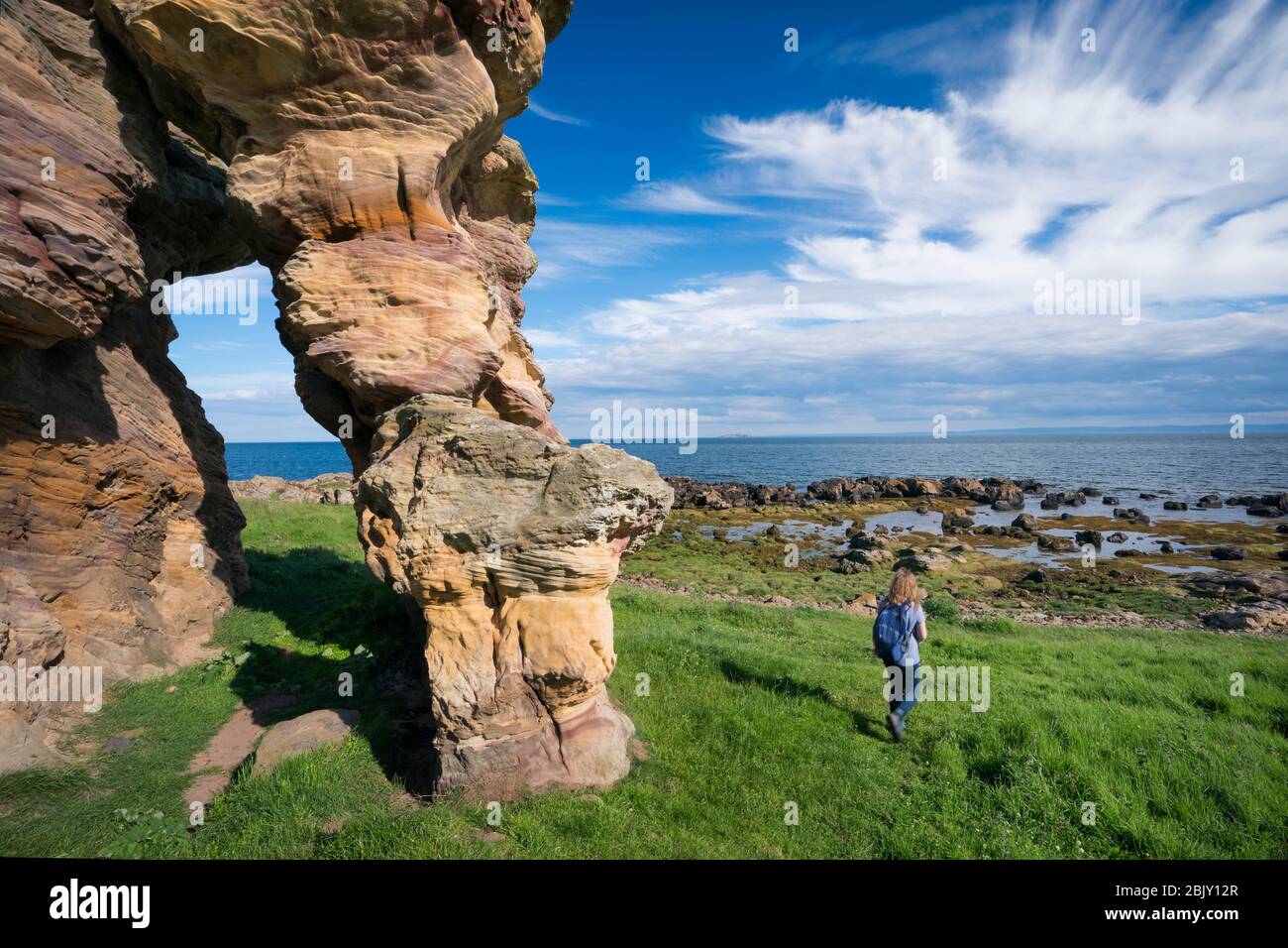 Una turista femenina camina por las cuevas Caiplie, o calas, formaciones rocosas a lo largo del Mar del Norte en el sendero costero Fife, Crain, Escocia, Europa Foto de stock