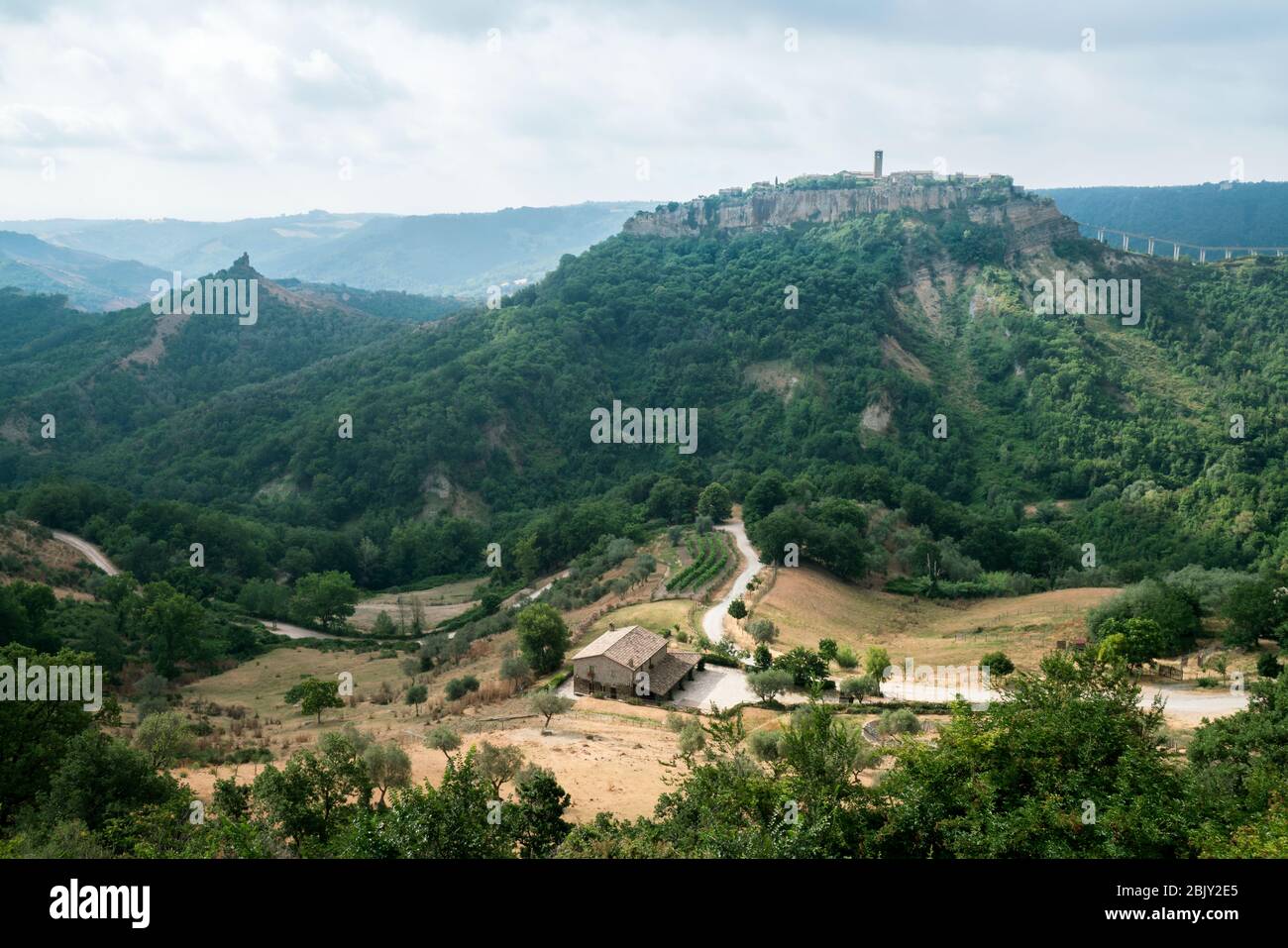 Vista distante de Cività di Bagnoregio más allá de las granjas locales. Civita Bagno, un antiguo pueblo etrusco en la cima de una colina, encaramado en la cima de una roca volcánica de tufta en el sur Foto de stock
