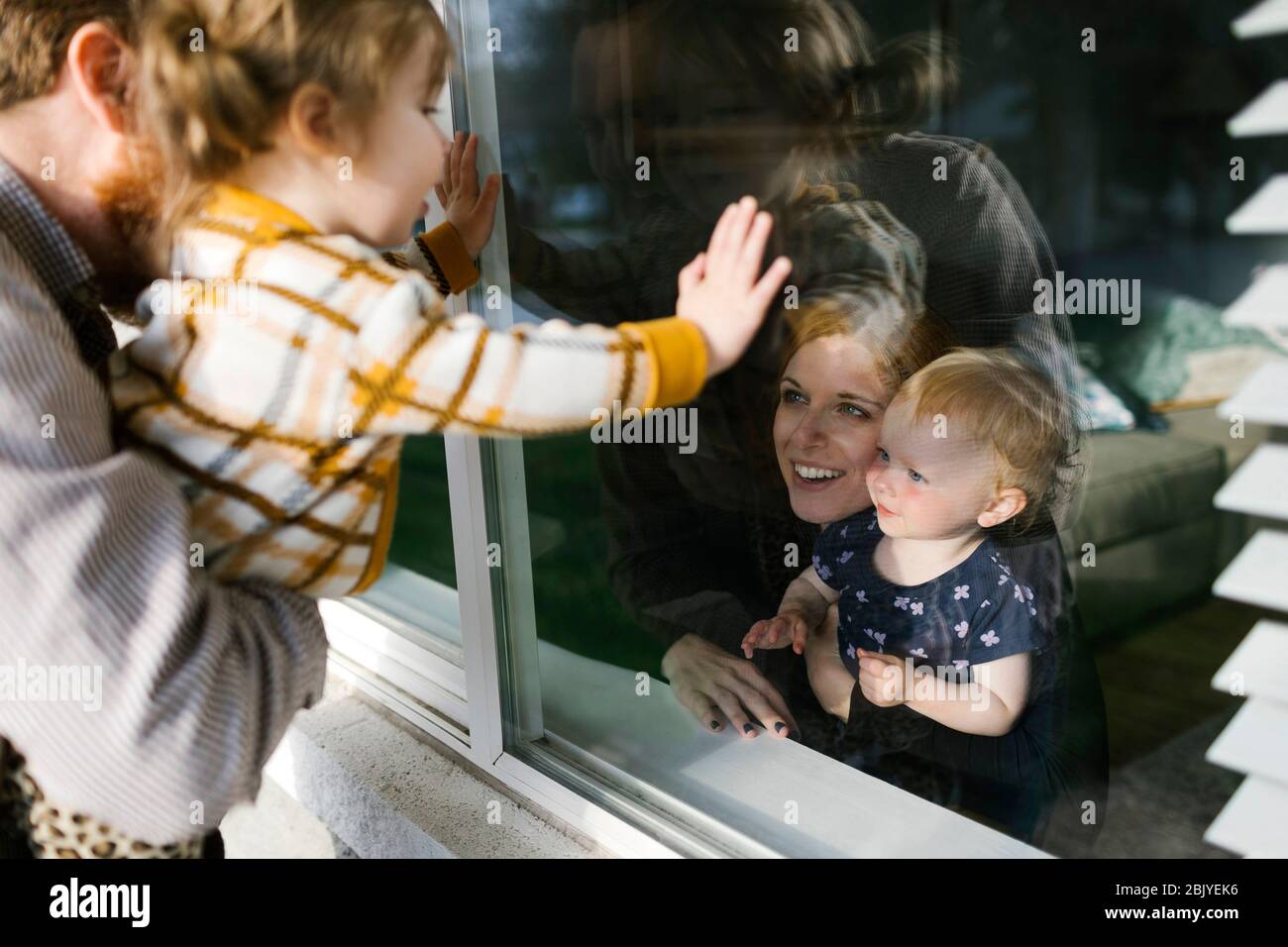 Familia con hijas (2-3) visitando a través de la ventana Foto de stock