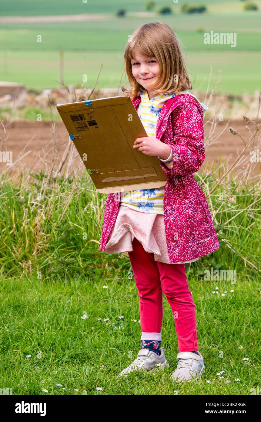 East Lothian, Escocia, Reino Unido. 1 de mayo de 2020. Escolarización en el hogar: Alice, de 5 años de edad, es estudiante de primaria 1. Ella trabaja en una tarea de aritmética al aire libre en la carretera aprendiendo cómo contar, coches, ciclistas, peatones, tractores y camiones Foto de stock