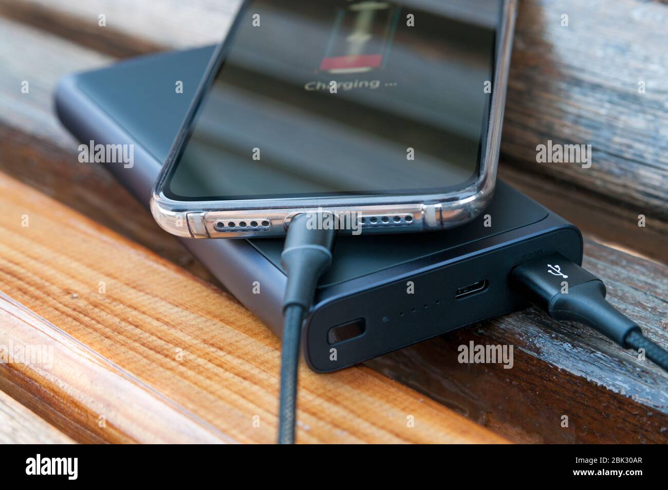 El smartphone moderno se carga desde la fuente de alimentación sobre el fondo de madera. Concepto de tecnología moderna. Enfoque selectivo. Foto de stock