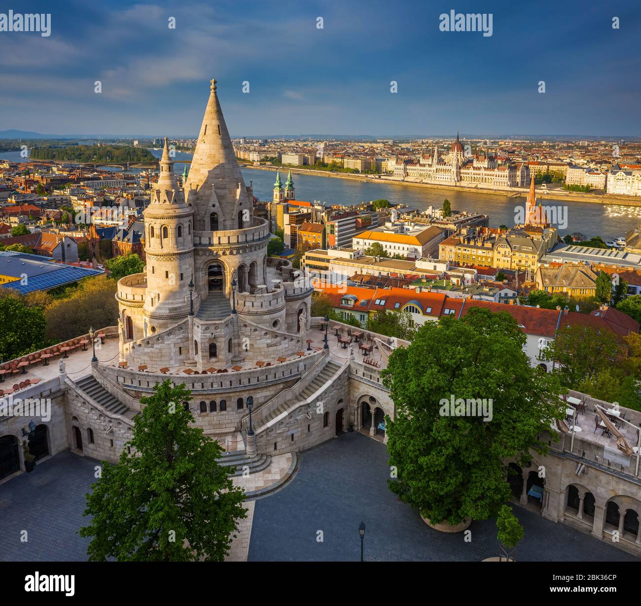 Budapest, Hungría - Vista aérea del famoso Bastión de los pescadores al atardecer con el edificio del Parlamento al fondo. Luz del sol cálida, cielo azul, no hay gente Foto de stock
