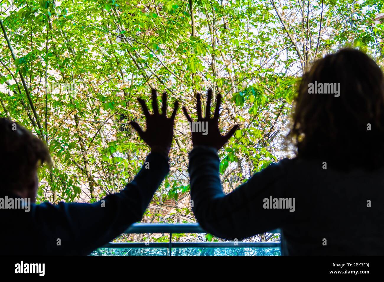 Mujeres en confinamiento con las manos en el panel de la ventana, mirando a la calle Foto de stock