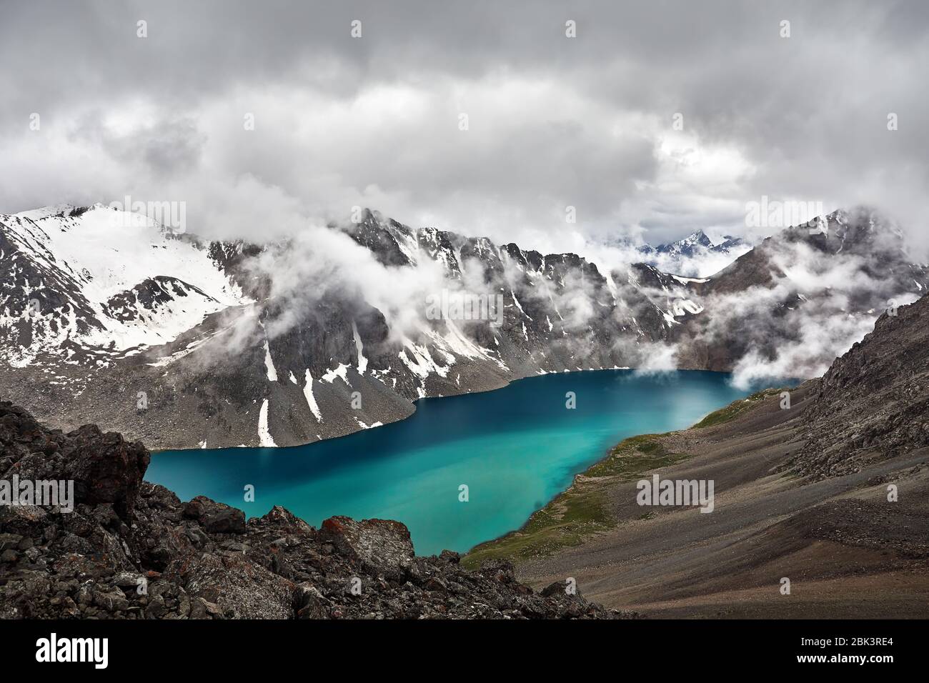Hermoso paisaje de turquesa Ala-Kul lago en las montañas Tien Shan, con blancas nubes de niebla en Karakol, parque nacional de Kirguistán Foto de stock