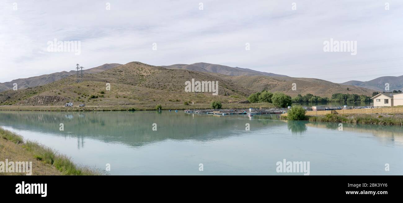 Paisaje con piscifactoría flotante de salmón en el brazo de Wairepo del lago Ruataniwha con laderas estériles en el fondo, rodada en la brillante luz de primavera nublado cerca de T. Foto de stock