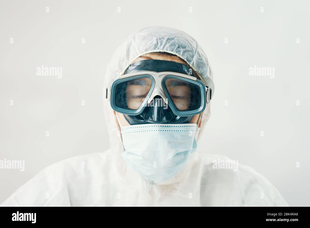Médico muy cansado con los ojos cerrados. Hombre profesional en traje con capucha para protección contra riesgos biológicos Foto de stock