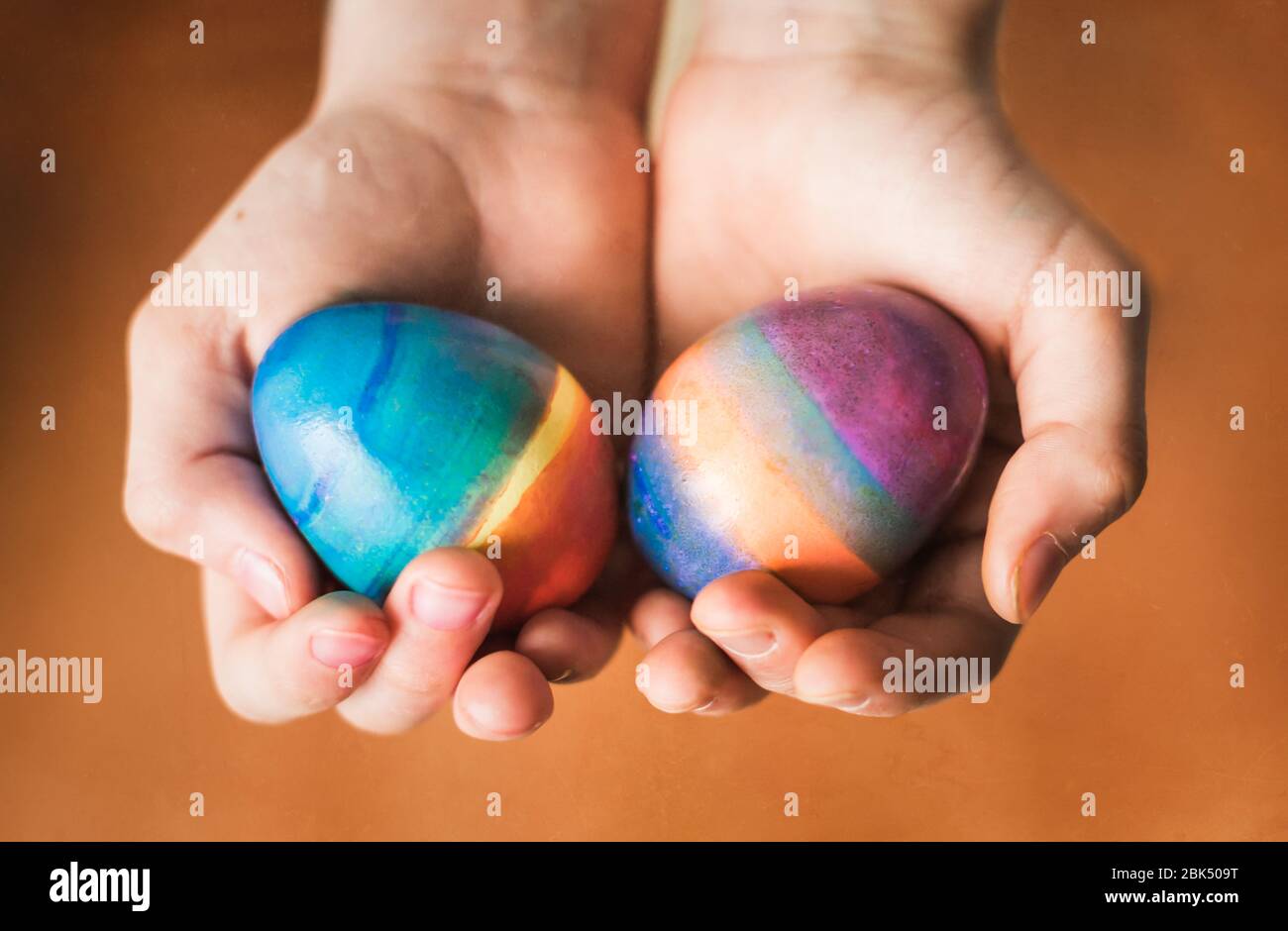 Primer plano de manos sosteniendo dos huevos de Pascua de colores brillantes. Foto de stock