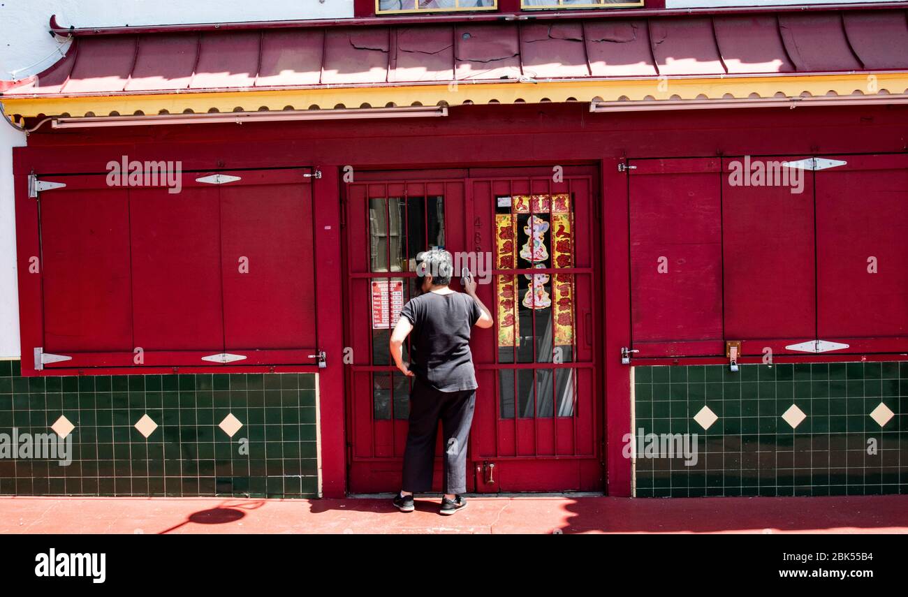 Mujer cierra la puerta en su tienda en Chinatown en el centro de los Ángeles durante el brote de coronavirus Foto de stock