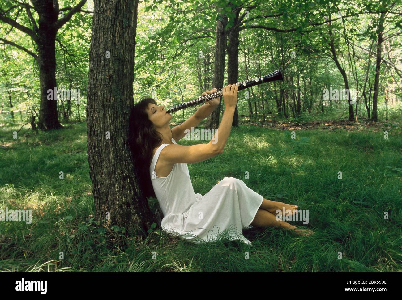 Mujer con un vestido blanco jugando el clarinete en un bosque de verano. Foto de stock